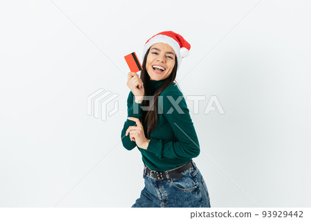 Joyful young woman wearing santa hat holding plastic credit card Joyful young woman wearing santa hat holding plastic credit card 93929442
