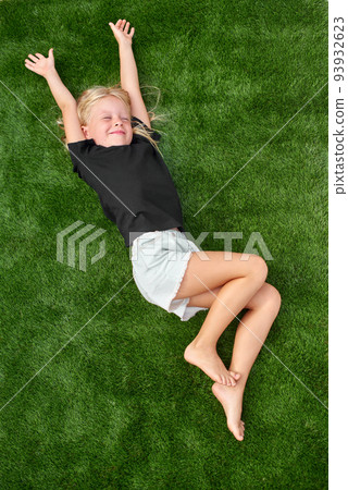Pretty blonde girl with closed eyes lying and stretching on green grass. Mock up black t shirt. Top view. Pretty blonde girl with closed eyes lying and stretching on green grass. Mock up black t shirt. Top view. 93932623