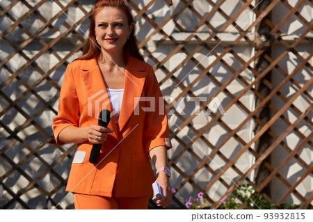 TV presenter, karaoke host. Young woman in an orange pantsuit with a microphone TV presenter, karaoke host. Young woman in an orange pantsuit with a microphone 93932815