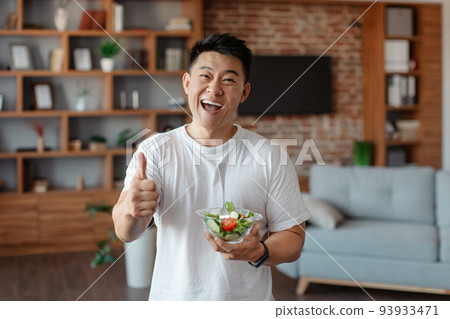 Fitness nutrition. Happy asian mature man holding bowl with fresh vegetable salad and showing thumb up 93933471