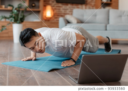 Asian mature man doing push-ups and looking at laptop, having online fitness class from home, selective focus 93933560