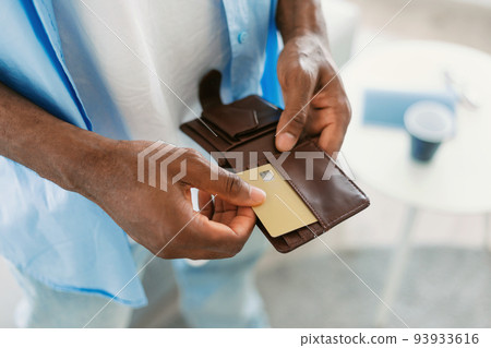 Unrecognizable black guy taking out credit card from his wallet, standing at home, closeup, copy space Unrecognizable black guy taking out credit card from his wallet, standing at home, closeup, copy space 93933616