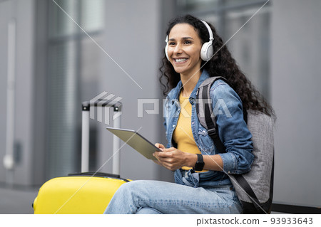 Happy young lady tourist using digital pad and wireless headphones 93933643