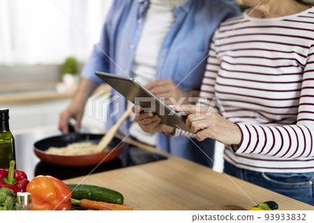 Senior Couple Using Digital Tablet In Kitchen While Cooking Food 93933832