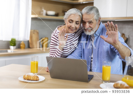 Happy senior spouses making video call with laptop in kitchen during breakfast 93933836
