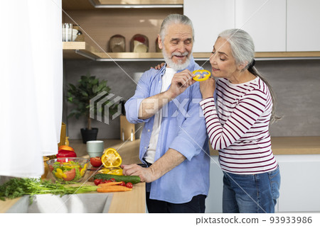 Portrait Of Happy Senior Spouses Cooking Food In Kitchen Together 93933986