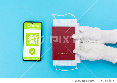 Hands in protective gloves give a passport with mask. Cellphone screen with an electronic health passport with qr-code. Flat lay. Concept of Covid-19 test for travel Hands in protective gloves give a passport with mask. Cellphone screen with an electronic health passport with qr-code. Flat lay. Concept of Covid-19 test for travel 93934107