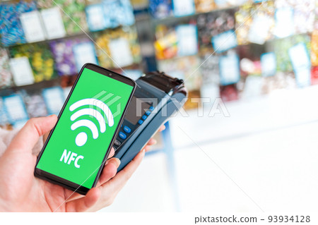 Women's hands are held by a payment terminal and a man pays for a purchase using a smartphone.On the phone screen, the wi-fi network. Copy space. The concept of NFC, business and banking transactions 93934128