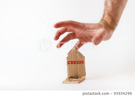 Bank investments and risks. a man's hand reaches for a mousetrap with a cardboard schematic house, with the inscription CREDIT. Copy space Bank investments and risks. a man's hand reaches for a mousetrap with a cardboard schematic house, with the inscription CREDIT. Copy space 93934299