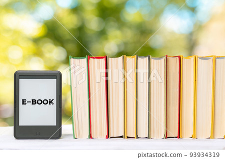 Knowledge. E-book reader and a stack of books. The park is blurred in the background. Copy space. Concept of education and electronic gadgets 93934319