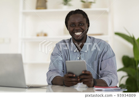 Happy Black Guy Using Digital Tablet While Sitting At Desk At Home 93934809