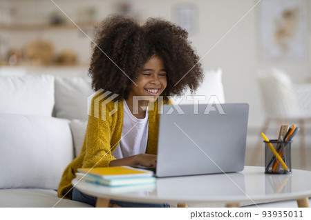 Smiling black school girl doing homework, using computer 93935011
