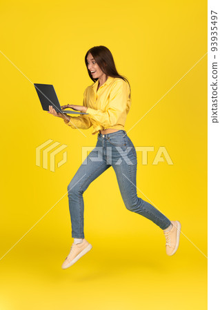Excited Lady Using Laptop Running Posing Over Yellow Background, Vertical Excited Lady Using Laptop Running Posing Over Yellow Background, Vertical 93935497