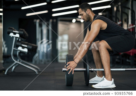 Young Black Male Athlete Adding Weight Plates On His Barbell At Gym Young Black Male Athlete Adding Weight Plates On His Barbell At Gym 93935766