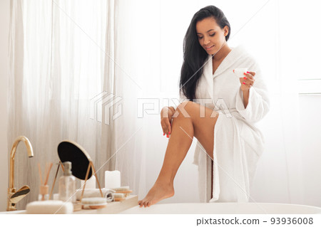 Pretty Female Applying Moisturizer On Legs Standing In Modern Bathroom 93936008