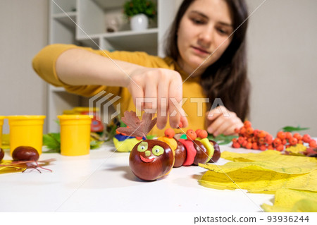 A woman decorates with viburnum berries an autumn craft caterpillar made of chestnuts and plasticine A woman decorates with viburnum berries an autumn craft caterpillar made of chestnuts and plasticine 93936244