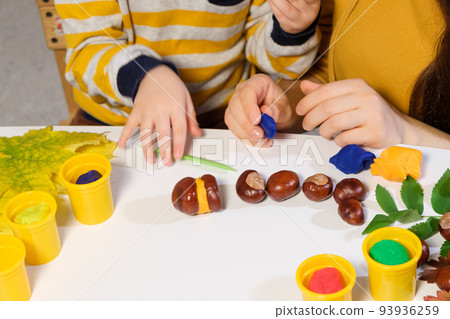 Mother and son sculpt autumn craft caterpillar from chestnuts and plasticine 93936259