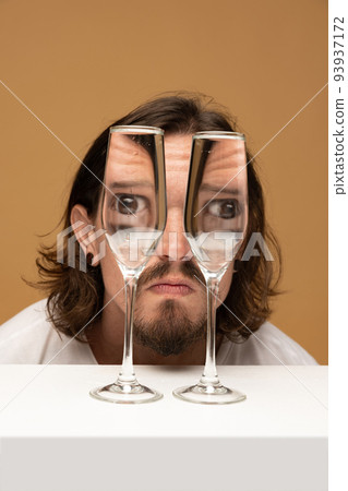 Happy man's face through wine glasses. Object distortion, optical illusion. Minimalistic contemporary art. Happy man's face through wine glasses. Object distortion, optical illusion. Minimalistic contemporary art. 93937172