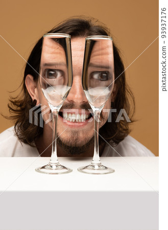 Happy man's face through wine glasses. Object distortion, optical illusion. Minimalistic contemporary art. Happy man's face through wine glasses. Object distortion, optical illusion. Minimalistic contemporary art. 93937176