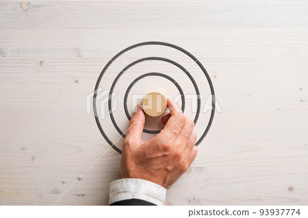 Hand of a businessman placing blank wooden cut circle in the middle of a target Hand of a businessman placing blank wooden cut circle in the middle of a target 93937774