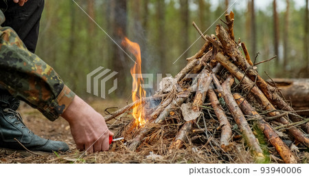 Man starts a fire in the forest using a lighter. Close-up of a man's hand lighting a fire with a lighter. Lighting a fire in the forest by a person. Low angle of a burning fire made of brushwood... 93940006