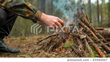 Low angle shot of a man is trying make a fire in the forest. Close-up of a man's hand lighting a campfire. Lighting a fire in the forest by a person. Low angle of a burning fire made of brushwood. 93940007