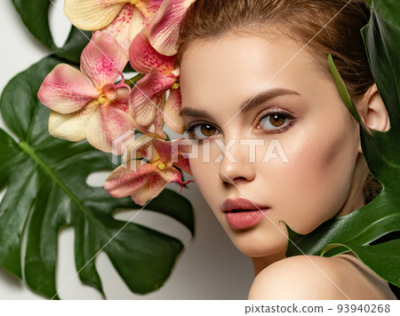Beautiful woman with green leave near face and body. Closeup girl's face with green leave. Pretty girl in Skin care beauty treatments concept. Model with pink tropical orchid near face. Brown makeup. 93940268