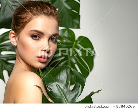Beautiful woman with green leave near face and body. Closeup girl's face with green leave. Pretty girl in Skin care beauty treatments concept. Model with big tropical leaf, posing, studio. Brown 93940269