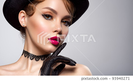 Art portrait of beautiful young woman with orange makeup in a black hat.  Closeup face of a sexy girl with red lipstick on lips. Stylish fashion portrait. Attractive model with a black gloves at 93940271