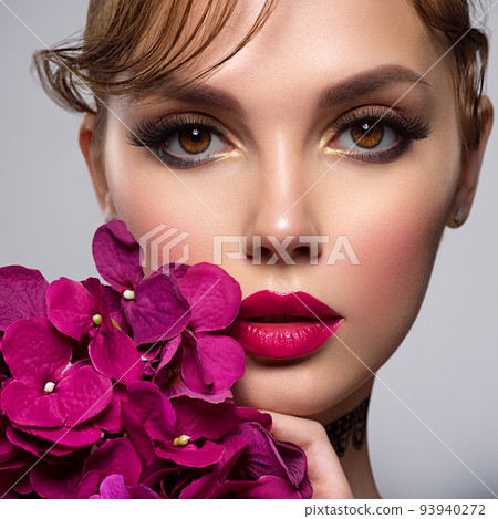 Beautiful white girl with purple flowers. Stunning brunette girl with big violet bouquet flowers. Closeup face of young beautiful woman with a healthy clean skin. Pretty woman with bright makeup 93940272