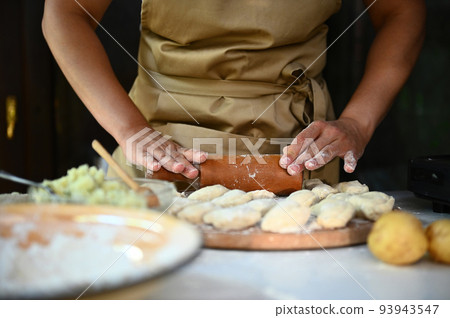 Close-up woman chef housewife in beige apron, rolls out the dough for dumpling with rolling pin, makes homemade vareniki Close-up woman chef housewife in beige apron, rolls out the dough for dumpling with rolling pin, makes homemade vareniki 93943547