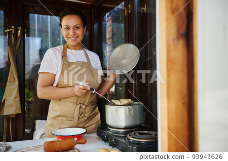 Pleasant woman, a housewife in beige chef's apron, taking out freshly brewed dumplings. Homemade culinary and traditions Pleasant woman, a housewife in beige chef's apron, taking out freshly brewed dumplings. Homemade culinary and traditions 93943626