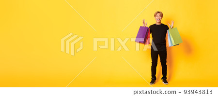 Full-length of happy handsome asian guy on shopping, holding bags and smiling, yellow background Full-length of happy handsome asian guy on shopping, holding bags and smiling, yellow background 93943813