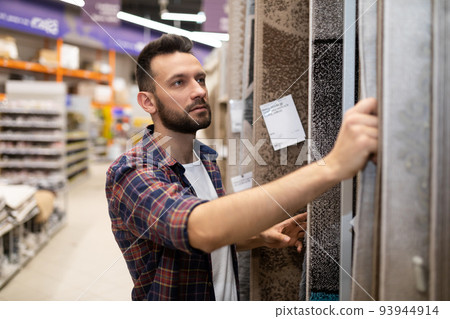 male buyer in a hardware store chooses carpet flooring 93944914
