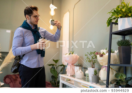 a customer of a fresh flower and potted plant store examines a small cactus in a flowerpot 93944929