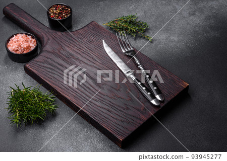 Wooden cutting board, salt, pepper, spices and herbs on a dark concrete background Wooden cutting board, salt, pepper, spices and herbs on a dark concrete background 93945277
