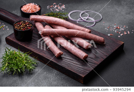 Raw sausages with spices on a wooden cutting board on a stone background with copy space for your text Raw sausages with spices on a wooden cutting board on a stone background with copy space for your text 93945294