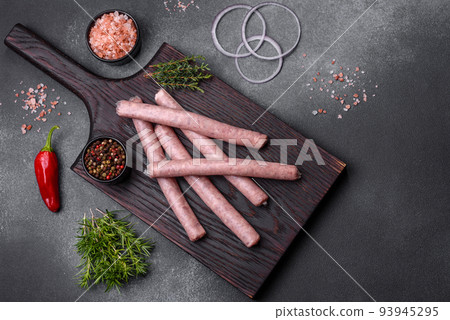 Raw sausages with spices on a wooden cutting board on a stone background with copy space for your text Raw sausages with spices on a wooden cutting board on a stone background with copy space for your text 93945295