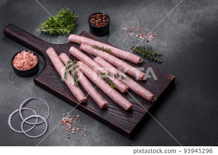 Raw sausages with spices on a wooden cutting board on a stone background with copy space for your text Raw sausages with spices on a wooden cutting board on a stone background with copy space for your text 93945296