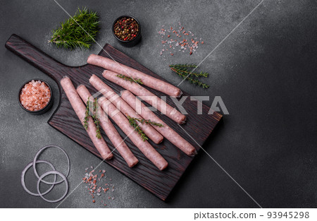 Raw sausages with spices on a wooden cutting board on a stone background with copy space for your text Raw sausages with spices on a wooden cutting board on a stone background with copy space for your text 93945298