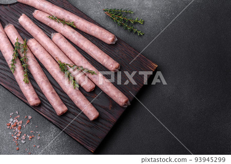 Raw sausages with spices on a wooden cutting board on a stone background with copy space for your text 93945299