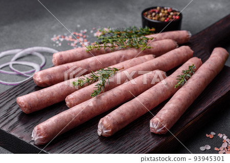 Raw sausages with spices on a wooden cutting board on a stone background with copy space for your text Raw sausages with spices on a wooden cutting board on a stone background with copy space for your text 93945301