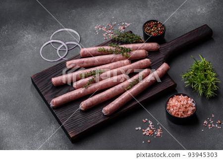 Raw sausages with spices on a wooden cutting board on a stone background with copy space for your text 93945303