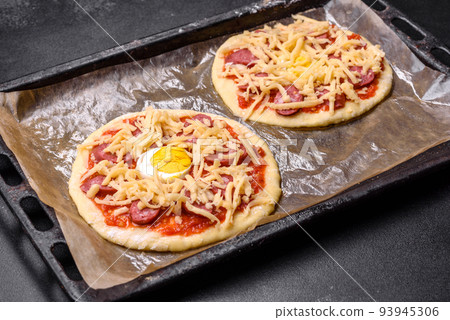 Homemade pizza with sausages, tomatoes, cheese, spices and herbs on a wooden cutting board Homemade pizza with sausages, tomatoes, cheese, spices and herbs on a wooden cutting board 93945306