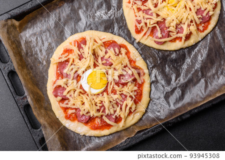 Homemade pizza with sausages, tomatoes, cheese, spices and herbs on a wooden cutting board Homemade pizza with sausages, tomatoes, cheese, spices and herbs on a wooden cutting board 93945308