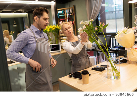 A flower shop owner teaches her intern how to assemble a fresh flower bouquet. A flower shop owner teaches her intern how to assemble a fresh flower bouquet. 93945666