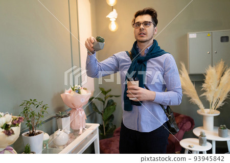 a man in a flower shop is interested in the cost of a cactus in a pot 93945842