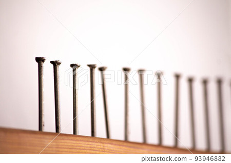 Several nails hammered into a wooden board close-up. The view is tilted diagonally focus 93946882