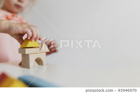 Adorable little child girl of preschooler age playing wooden building blocks at home or kindergarten. Toddler kid is stacking a tower from colourful cube toys on the table. Kids Play Room. Banner size 93946970
