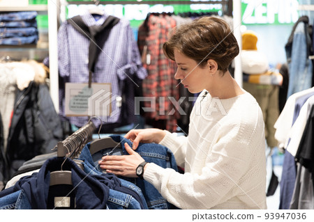 young woman chooses clothes in second hand young woman chooses clothes in second hand 93947036